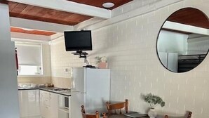 A dining area with a wooden table and chairs, a television mounted on the wall, and a kitchen in the background.