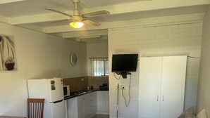 A bedroom with a bed, a desk, a chair, a TV, a wardrobe, and a kitchenette. - CABIN 2Q - Couple or single, motel style cabin (Thornton)