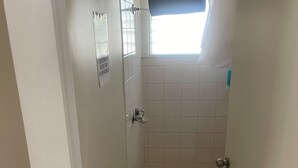 Ein kleines, gefliestes Duschbad mit einem Fenster über der Dusche, einer Tür mit Griff und einem Schild an der Wand.