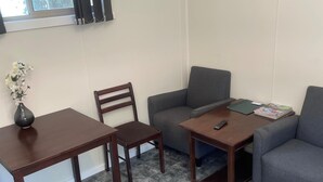 Ein Wohnzimmer mit einer Couch, einem kleinen Tisch, einem Sessel und einem Fenster mit Vorhängen.