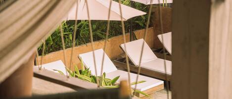 Een houten terras met lounge stoelen en parasols, omringd door groen.