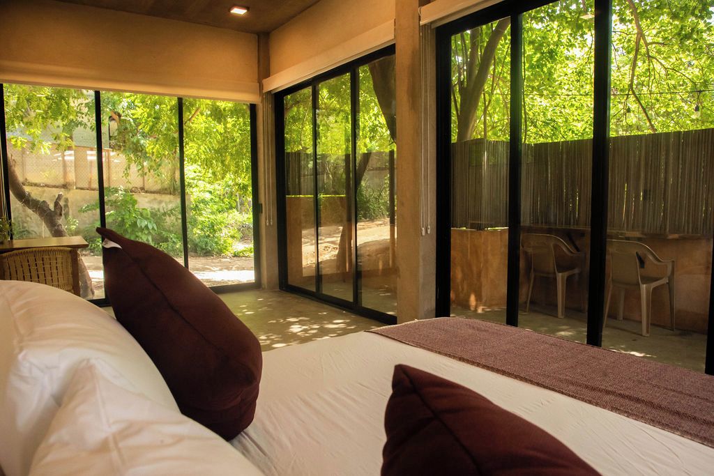 Un dormitorio con una cama grande, dos almohadas y vistas a un espacio exterior con sillas y una mesa a través de puertas de vidrio.