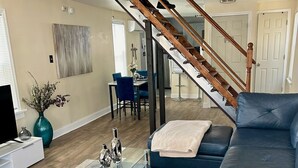 Un salon moderne avec un grand canapé d’angle, une table basse en verre et un escalier doté de rampes en bois.
