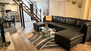 Un salon avec un canapé en cuir noir, une table basse en verre et un plancher en bois.