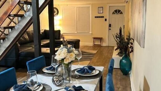 Un coin repas avec une table dressée pour quatre personnes, un escalier et, au fond, un salon.
