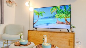 Una sala de estar con un televisor mostrando una escena de playa, un sofá, dos tazones de palomitas y una lata de bebida.