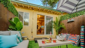 Un patio trasero con mesa, bebidas y aperitivos, un sofá y un parasol a rayas.