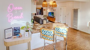 Un moderno vestíbulo de hotel con un mostrador de recepción, un letrero de neón que dice "Ocean Beach" y un área de descanso con dos sillas y una mesa.