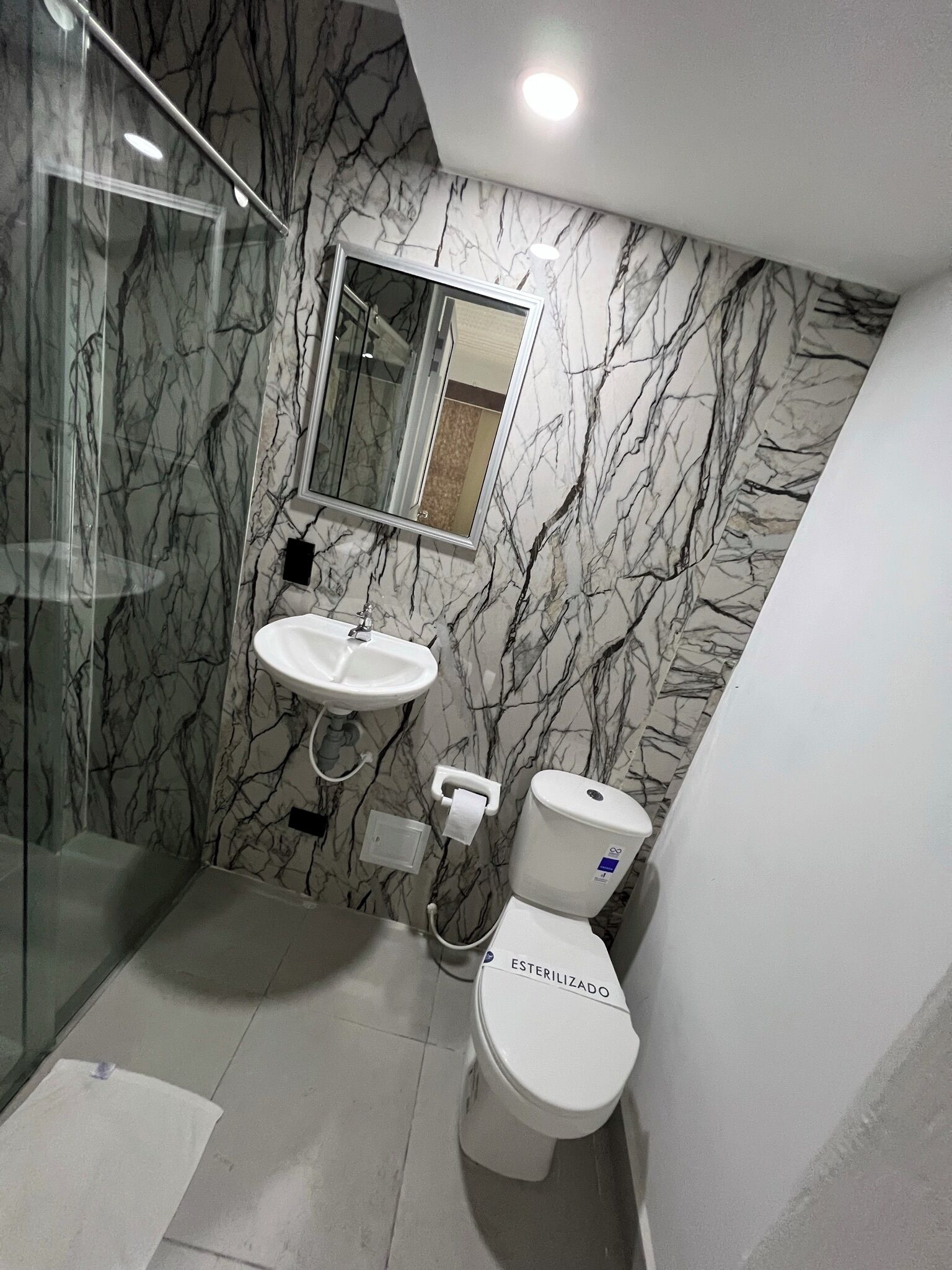 A bathroom with a marble wall, a glass shower enclosure, a sink, and a toilet.
