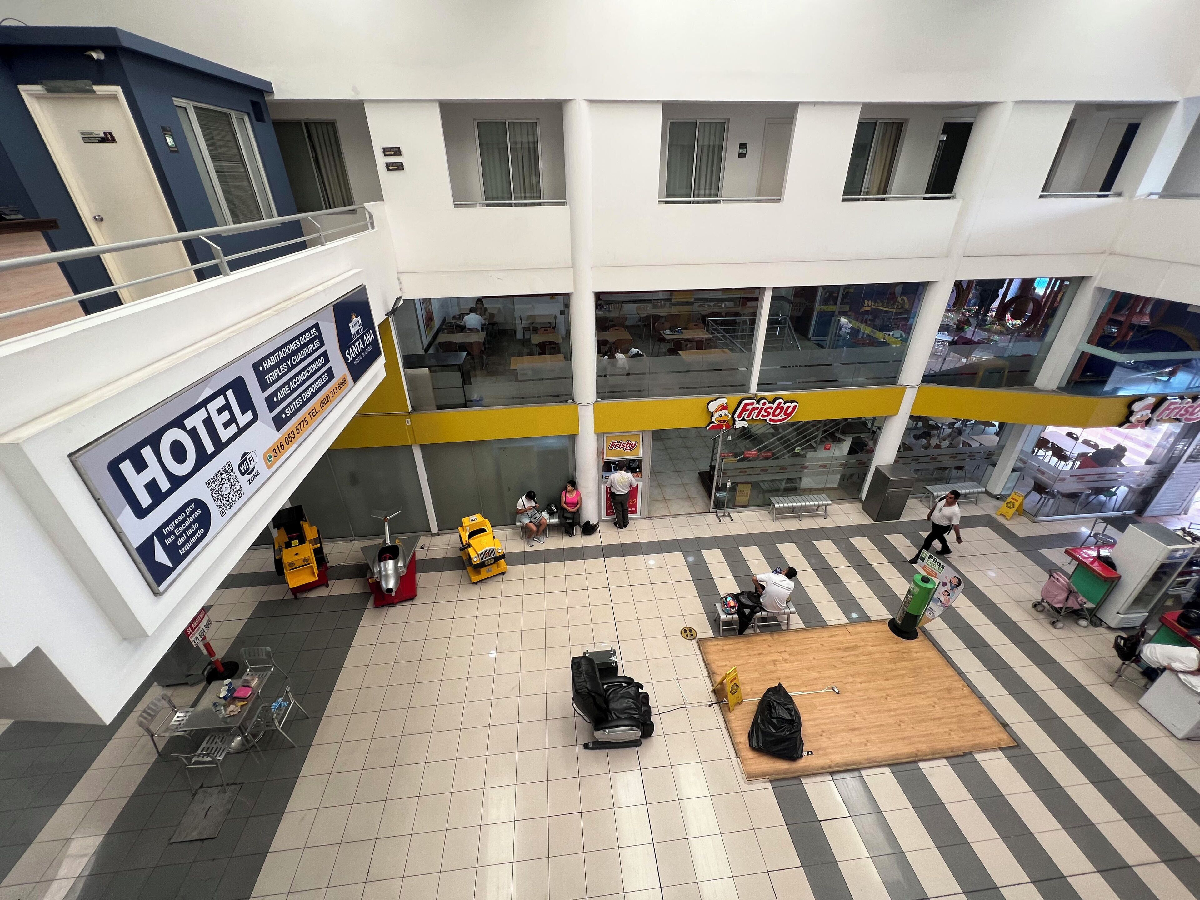 A hotel lobby with a sign for a hotel, a Frizzy fast-food restaurant, and a seating area with tables and chairs.