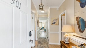 Un couloir avec une porte portant l’inscription « 301 », une lampe, une table décorative et un tableau représentant un papillon accroché au mur.