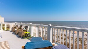 Un balcon avec des fauteuils en osier, une petite table et une vue sur la plage et l’océan.