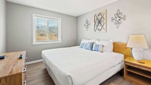 Une chambre avec un grand lit, un bureau et une table de chevet. Des œuvres d’art décoratives sont accrochées au mur au-dessus du lit.