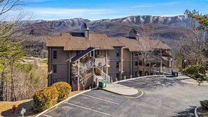 Un immeuble à plusieurs étages, avec un parking devant, entouré d’arbres et avec des montagnes en arrière-plan.