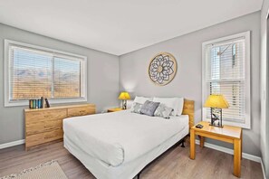 Une chambre à coucher avec un grand lit, deux tables de chevet avec des lampes, une commode en bois et une œuvre d’art murale.