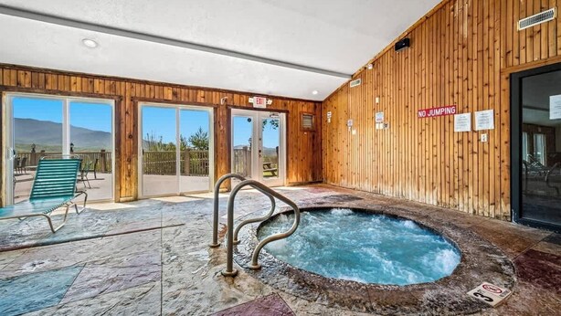 Un espace piscine intérieure doté d’un jacuzzi, de murs en bois et offrant une vue dégagée sur l’extérieur.