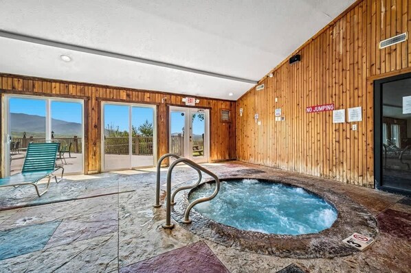 An indoor pool area with a hot tub, wooden walls, and a clear view of the outdoors.