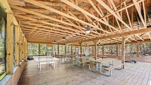 Un espace pique-nique abrité, doté de bancs et de tables en bois, et entouré de grandes fenêtres.
