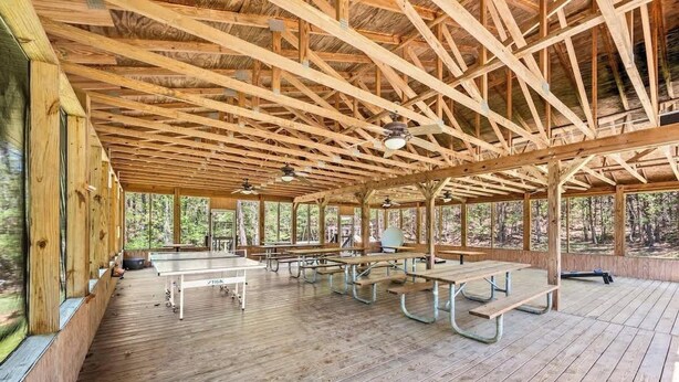 Un espace pique-nique abrité, doté de bancs et de tables en bois, et entouré de grandes fenêtres.