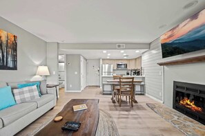 Ein modernes Wohnzimmer mit Kamin, einem Essbereich und einer Küche im Hintergrund.