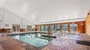 Une piscine intérieure dotée d’un jacuzzi, de chaises longues et offrant une vue sur l’extérieur.
