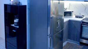 Een moderne keuken met een roestvrijstalen koelkast, magnetron en oven. Er is een zwart kastje en een klein plankje met een vaas.