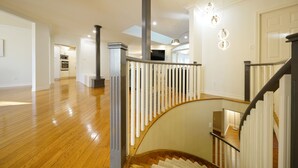 Un intérieur spacieux avec un plancher en bois, un escalier en colimaçon doté d’une rampe en métal, et un coin cuisine à l’arrière-plan.