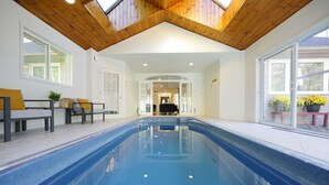 Une piscine intérieure dotée d’un plafond en bois et de portes vitrées donnant sur un espace extérieur agrémenté de plantes en pot.