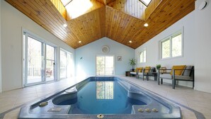 Une piscine intérieure spacieuse, dotée d’un plafond en bois et de grandes fenêtres.
