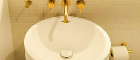 A bathroom with a white sink, gold faucets, and a toilet paper holder.