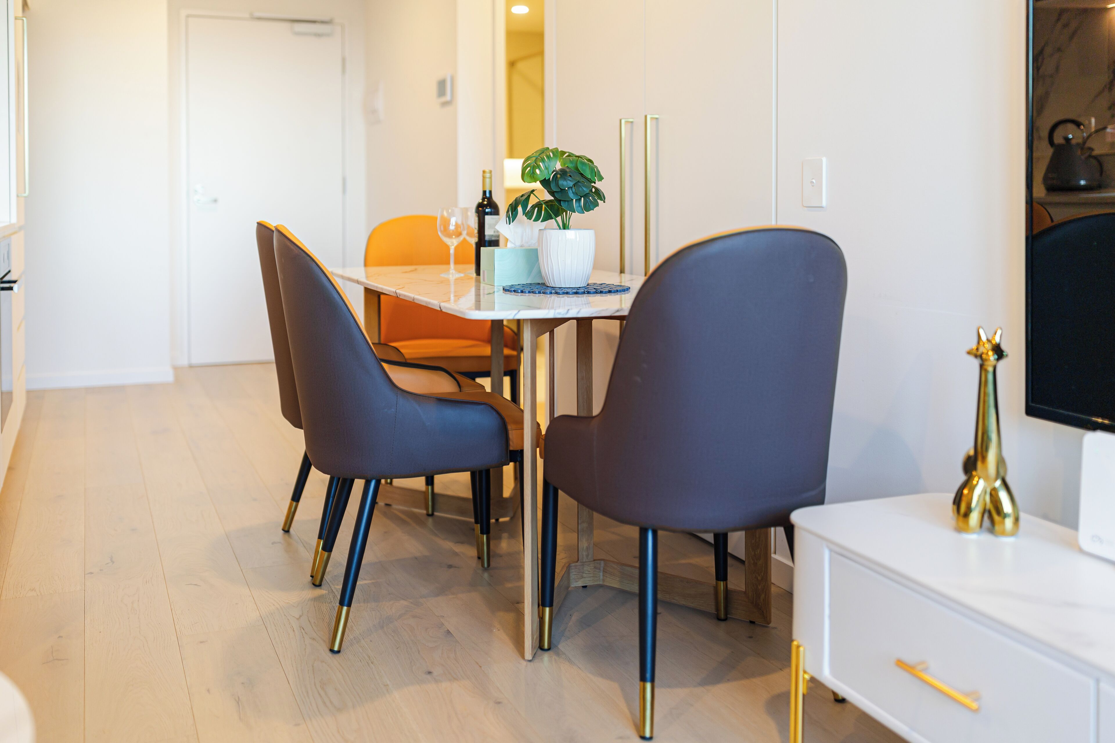 A modern dining area with a white table, blue chairs, and a potted plant.