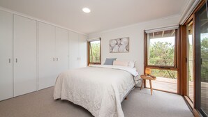 Une chambre avec un grand lit, une armoire et deux fenêtres donnant sur un paysage verdoyant.