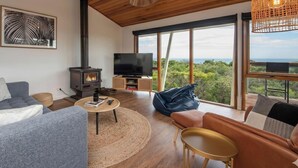 Un salon moderne doté d’une cheminée, d’un téléviseur et de grandes fenêtres offrant une vue sur le paysage.