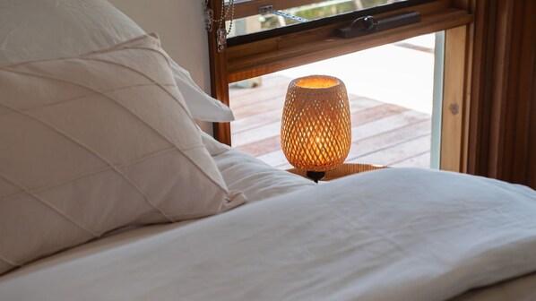 A bed with white bedding and a textured orange lamp on a wooden nightstand.