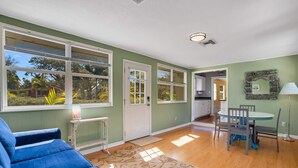 A living room with a blue sofa, a dining table with chairs, and a kitchen in the background. - Sea Board Pool Home - Monthly Vacation Rental (Clearwater)