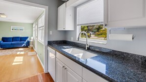 A modern kitchen with granite countertops, white cabinets, and a window with blinds. - Sea Board Pool Home - Monthly Vacation Rental (Clearwater)