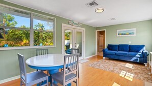 A dining area with a round table and chairs, a blue couch, and a view of greenery through large windows. - Sea Board Pool Home - Monthly Vacation Rental (Clearwater)