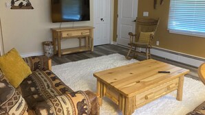 A living room with a sofa, a coffee table, a TV on a stand, a rocking chair, and a window with blinds. - Blocks from downtown and has that country feel. Nestle in Columbia Falls comfort (Columbia Falls)