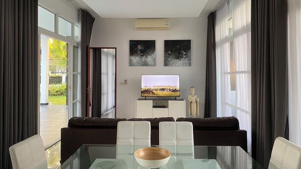 Un salon moderne avec une table à manger en verre, des chaises blanches, un téléviseur à écran plat et une statue.