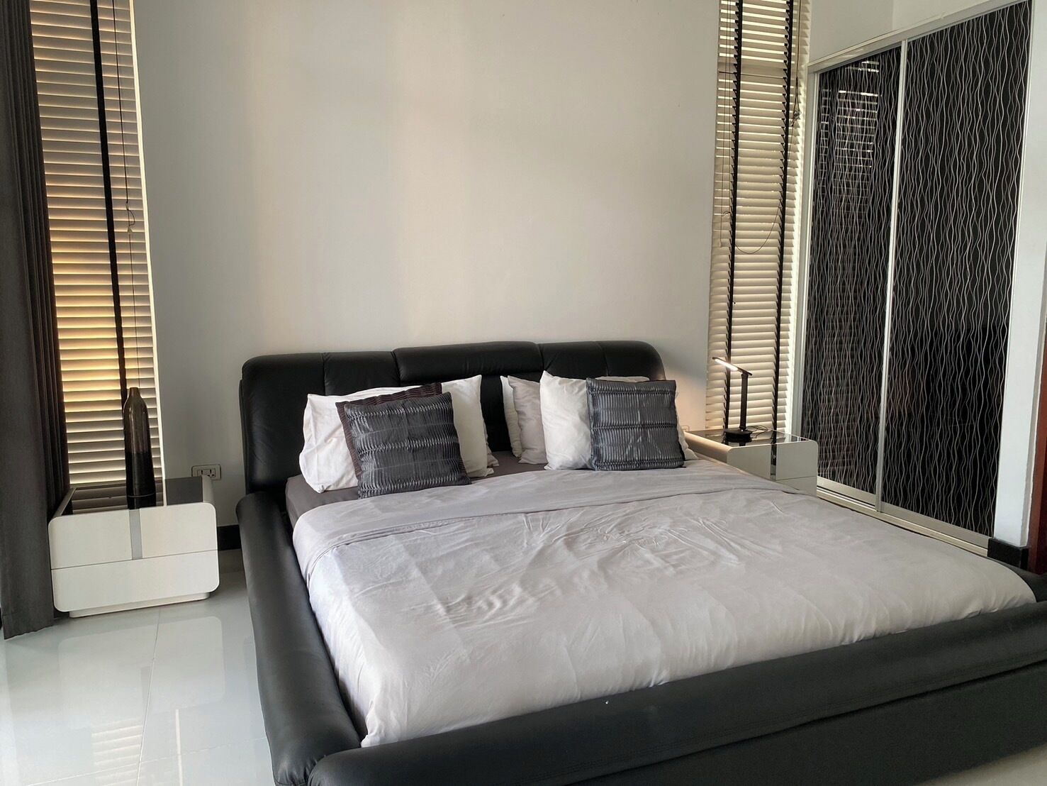 A modern bedroom with a black headboard, a large bed with white bedding, and a view through a window with blinds.