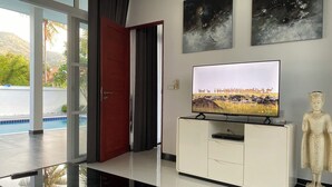 Un salon moderne avec un téléviseur posé sur un meuble blanc, une statue et deux tableaux abstraits accrochés au mur.
