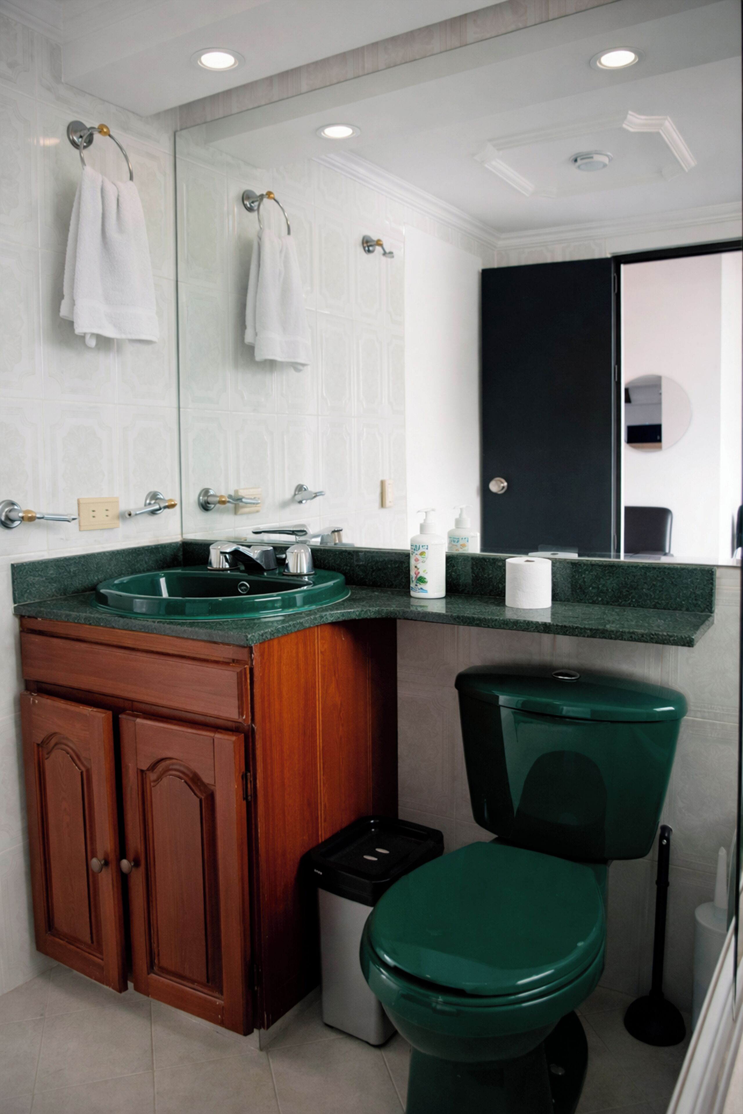 A bathroom with a green toilet, a sink with a green countertop, wooden cabinets, and a mirror above the sink.