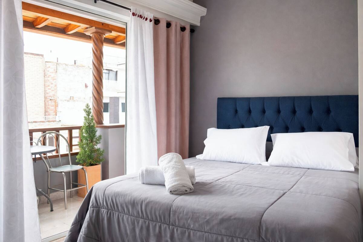 A hotel room with a bed, a balcony with a table and chairs, and a potted plant.