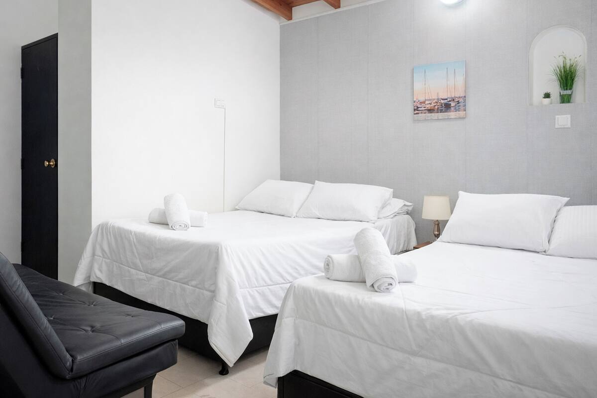 A hotel room with two beds, a black chair, a lamp, and a wall-mounted picture.