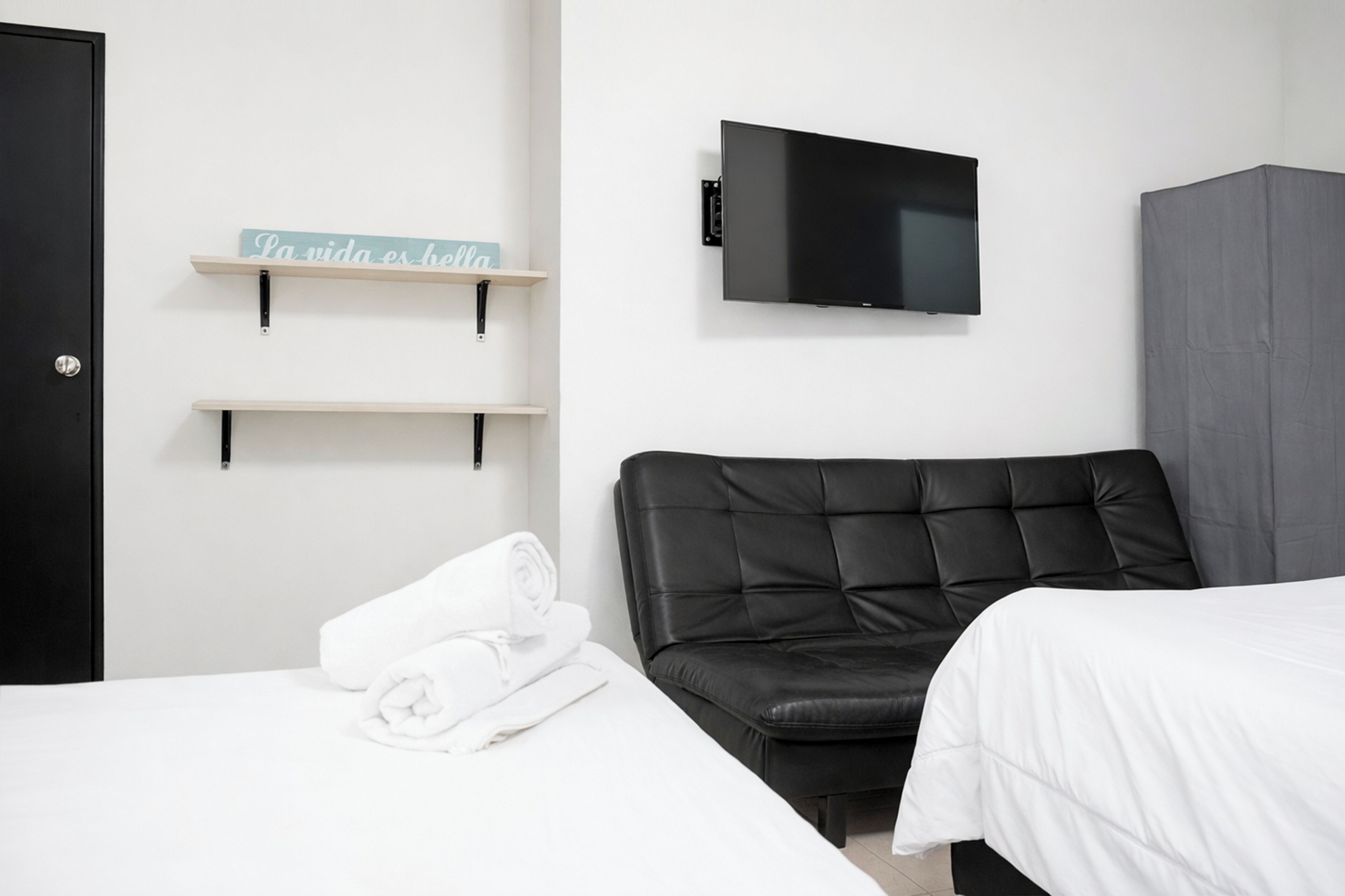 Une chambre d’hôtel comprenant un lit, un canapé en cuir noir, un téléviseur à écran plat fixé au mur et une armoire.