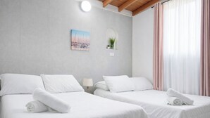 A hotel room with two beds, a painting, a potted plant, and a window with curtains. - Compostela Estadio (Medellín)