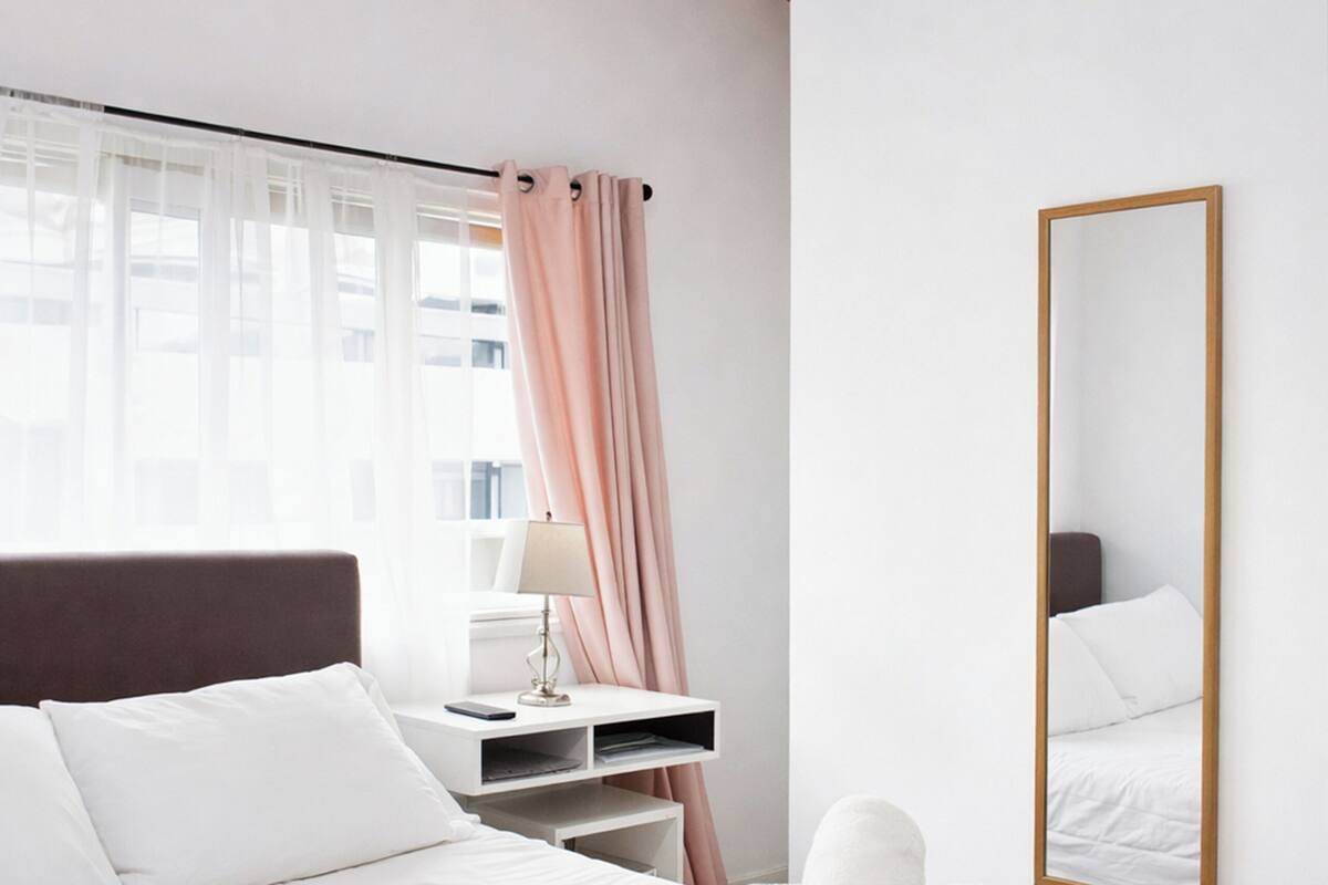 A hotel room with a bed, bedside table, lamp, and a large mirror.