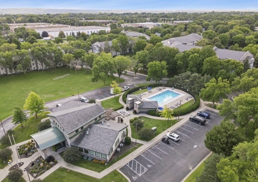 An aerial view of a residential area with a swimming pool, parking lot, and a building with a curved roof.