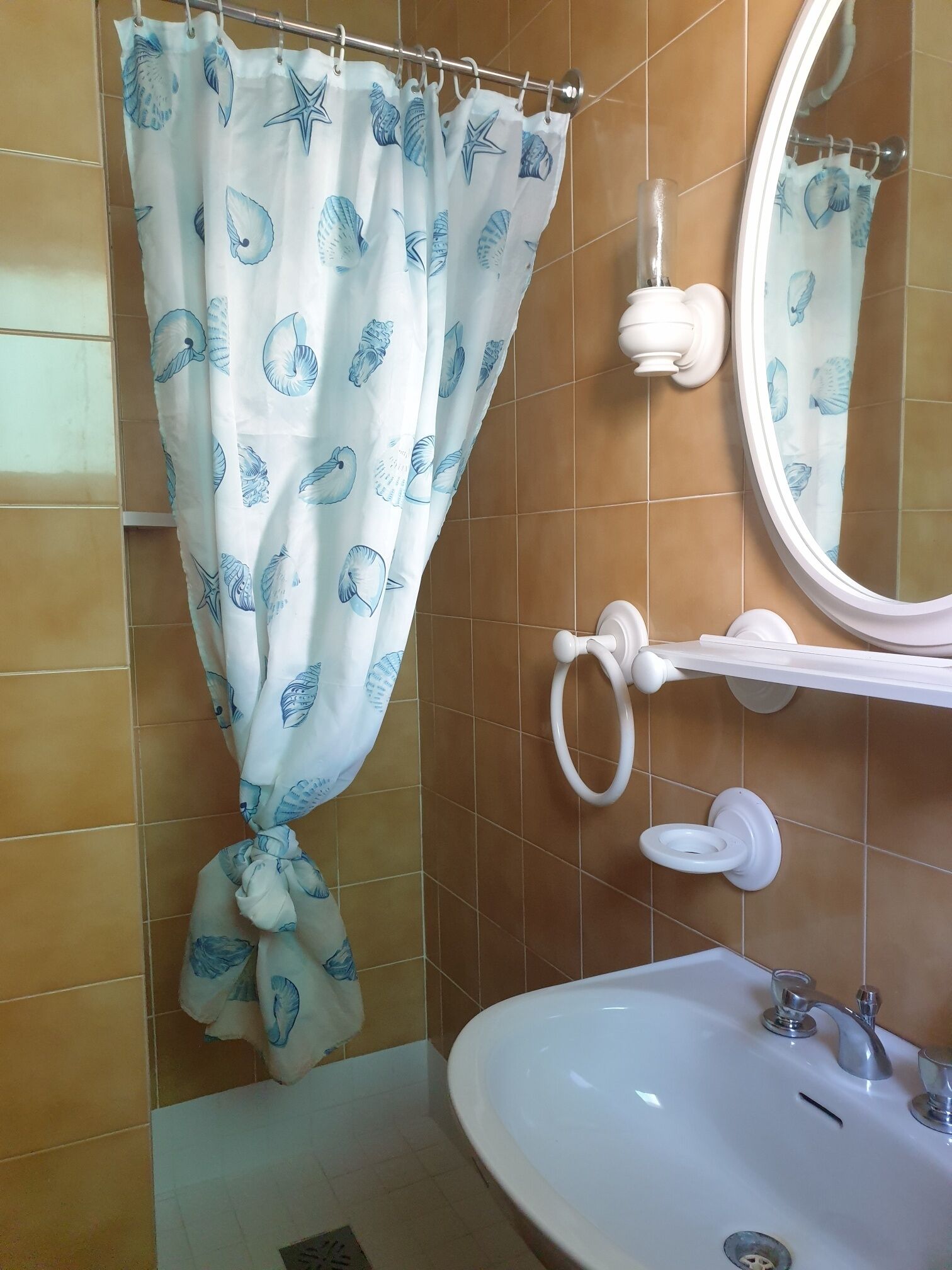 Un baño con lavamanos blanco, un espejo y una cortina de ducha con diseño de conchas marinas.