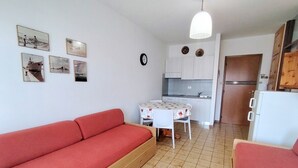 A compact living space with a red sofa, a small dining table with chairs, a kitchen area, and a refrigerator. - Calm Apartment Perfect for up to 4 Guests (San Michele al Tagliamento)